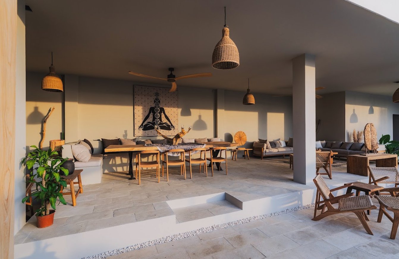 Open-air lounge and dining area with woven pendants and wellness tapestry at Selvamar